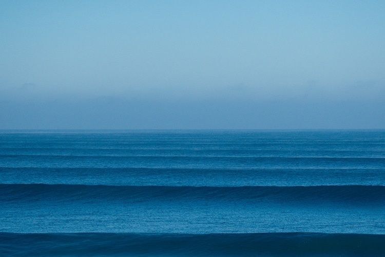 Parallel ocean swell lines rolling toward a flat horizon
