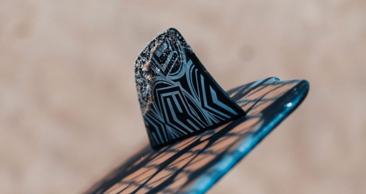 Close-up of a patterned surfboard fin with sand along its edge