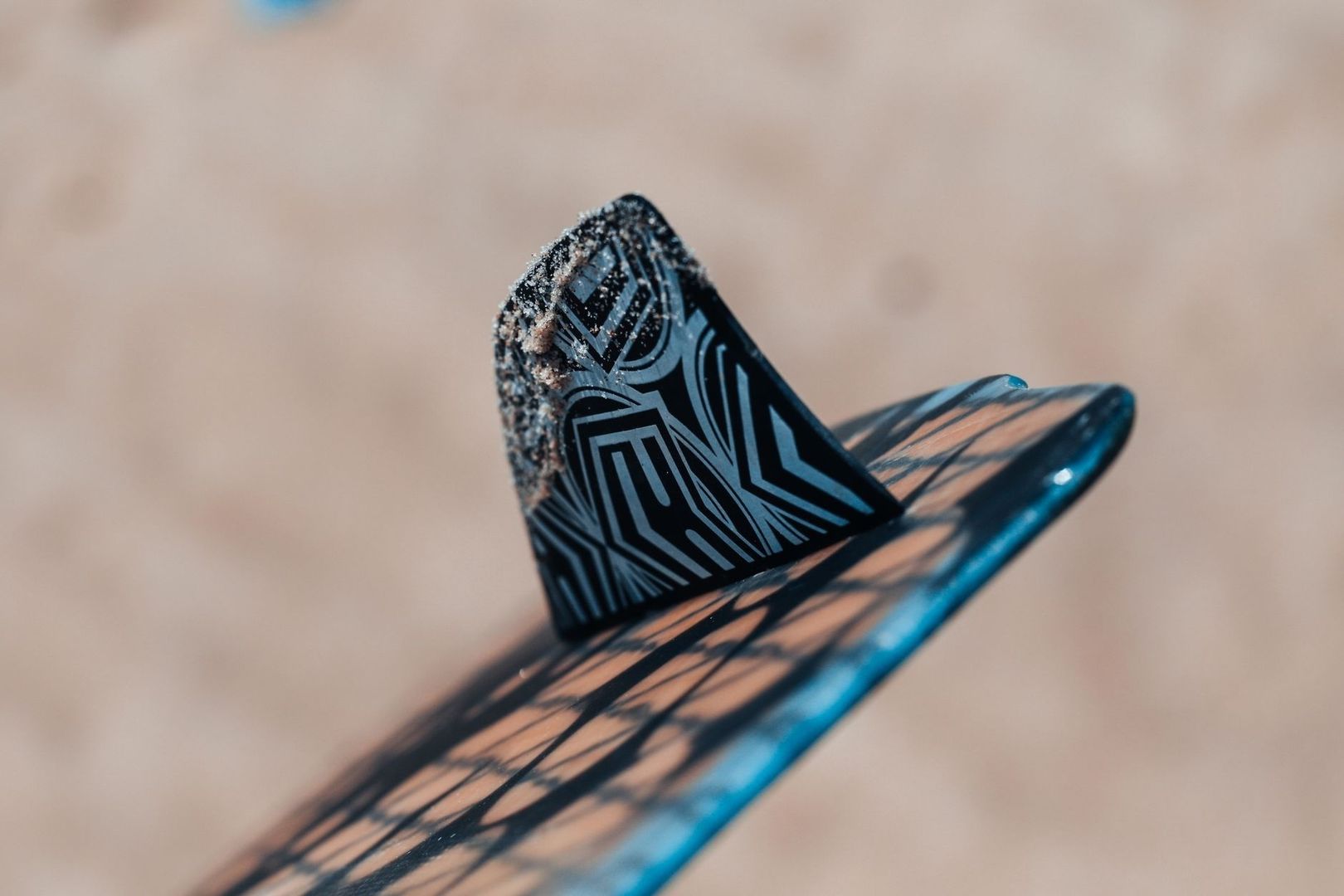 Close-up of a patterned surfboard fin with sand along its edge