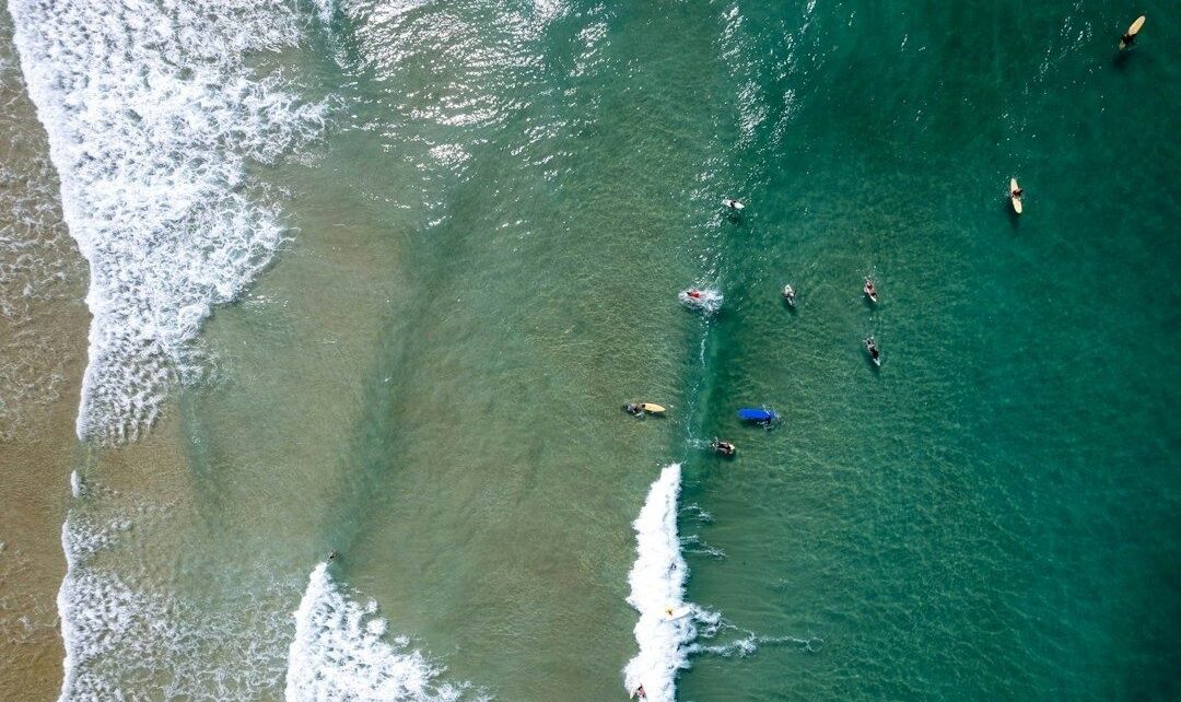 Aerial view of surfers positioning around shifting beach-break waves