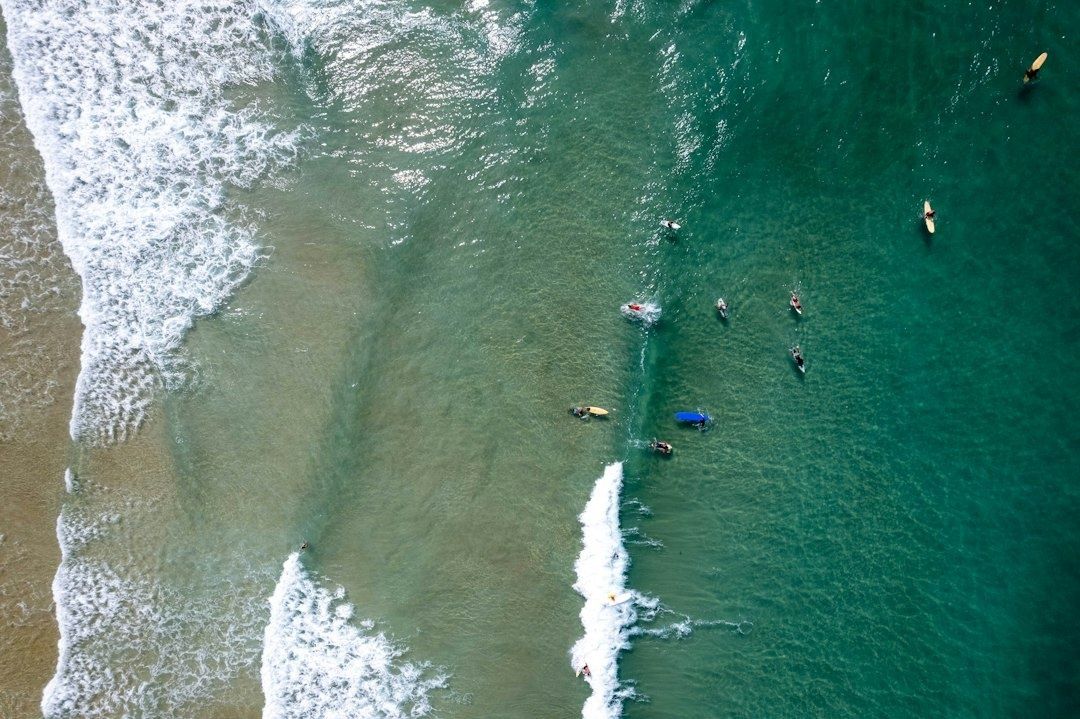 Aerial view of surfers positioning around shifting beach-break waves