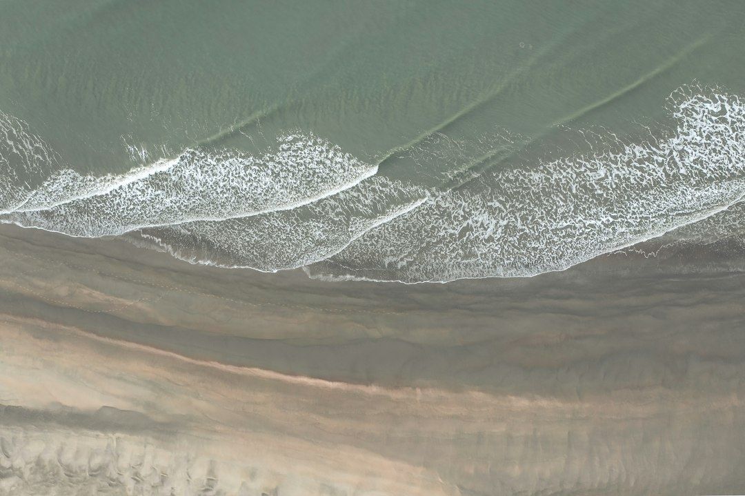 Aerial view of several shifting waves breaking along a sandy beach